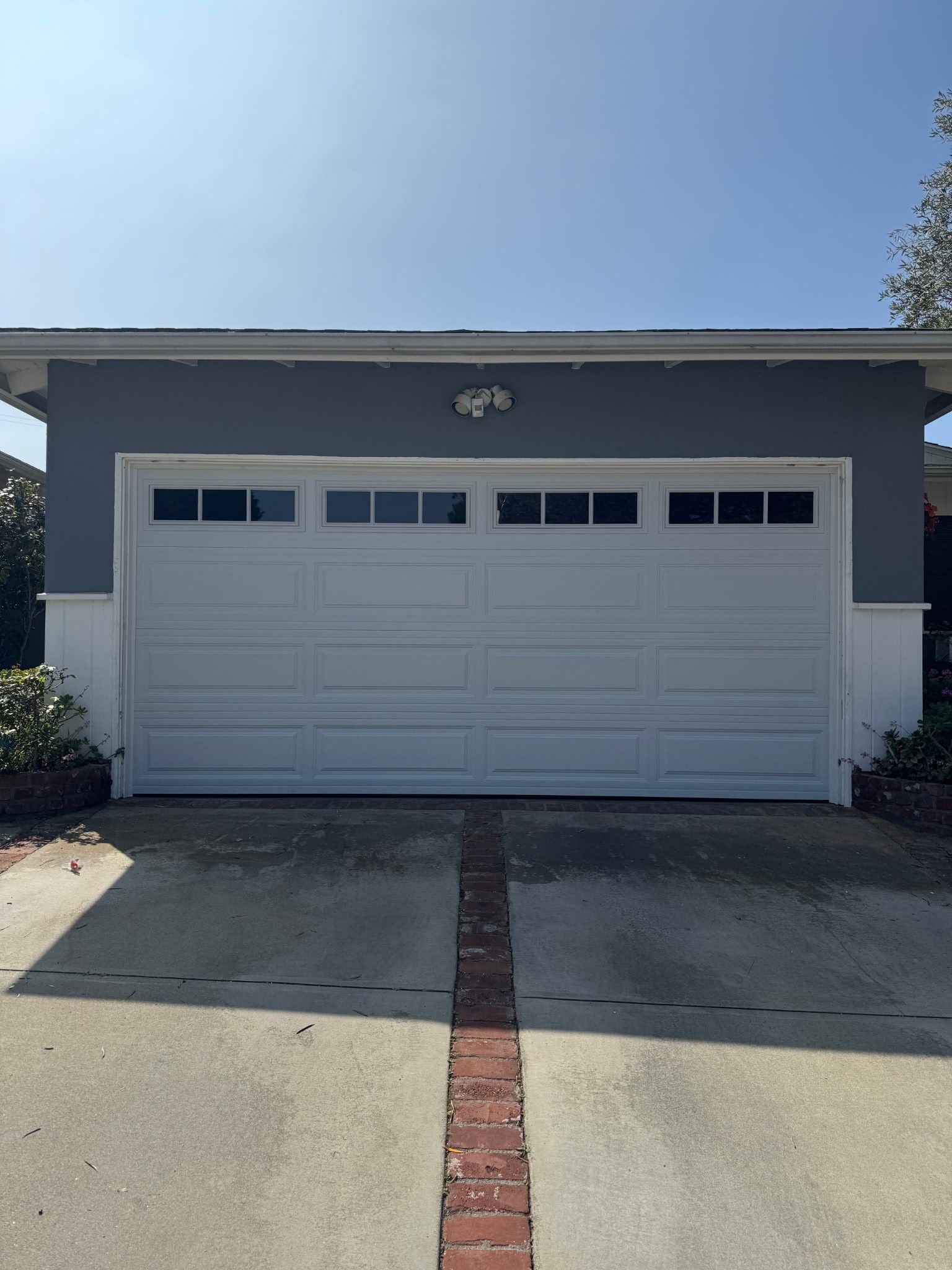 White garage door on a single-story house with a brick walkway and driveway under a clear blue sky