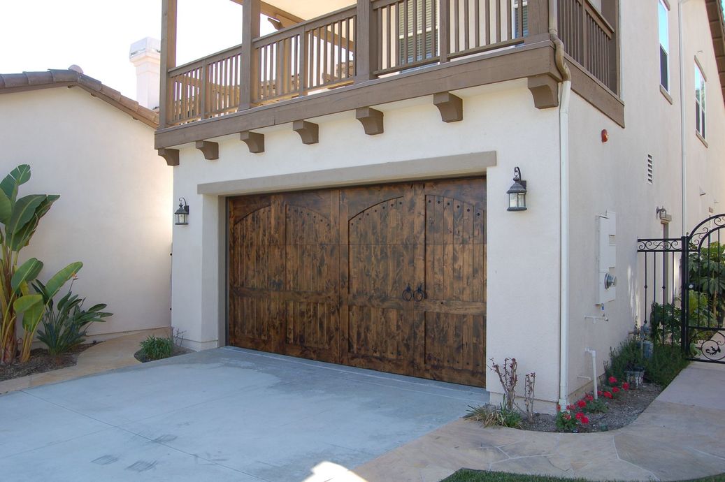 Residential garage with rustic wooden door beneath a balcony on a stucco house