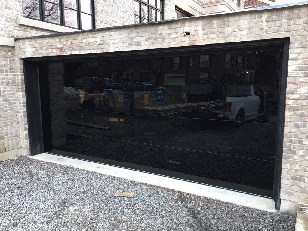 Black glass garage door set in a stone wall with gravel driveway in front