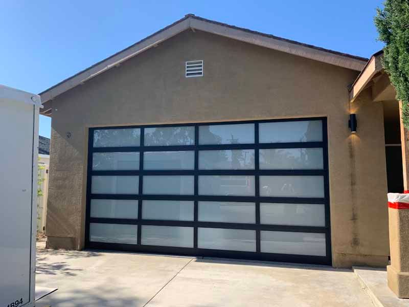 Single-story house with frosted glass garage door and tan stucco exterior under a blue sky