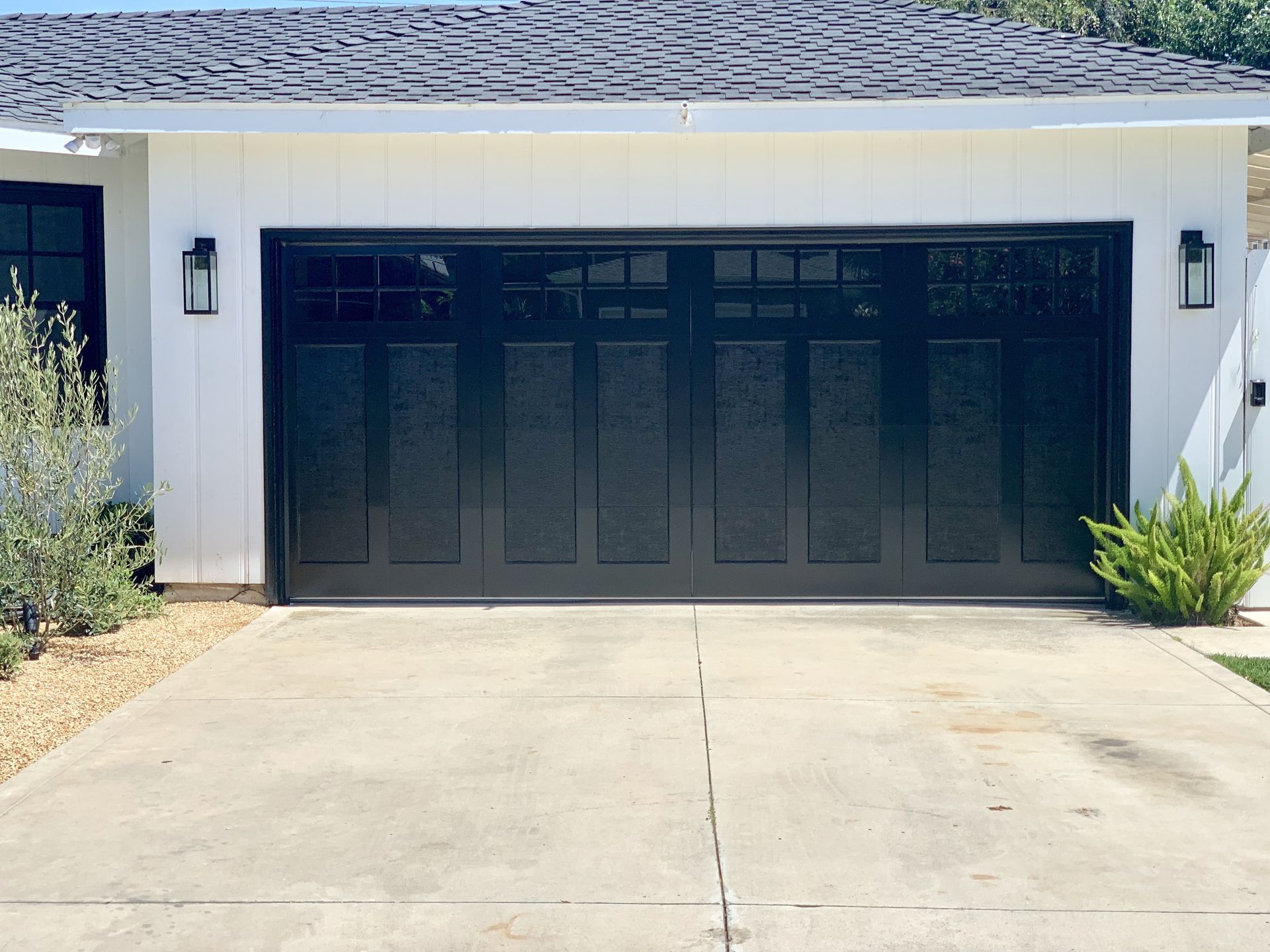 Two-car garage with dark doors and a concrete driveway in front of a white house
