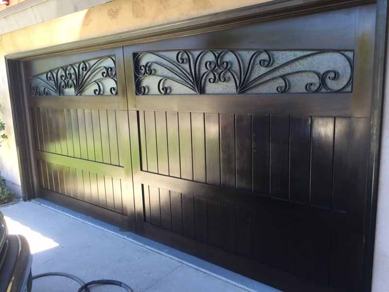 Black metal garage gate with decorative scrollwork panels in a sunlit driveway