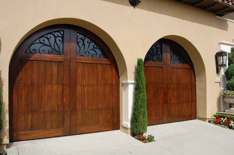 Two wooden arched garage doors on a beige stucco house facade