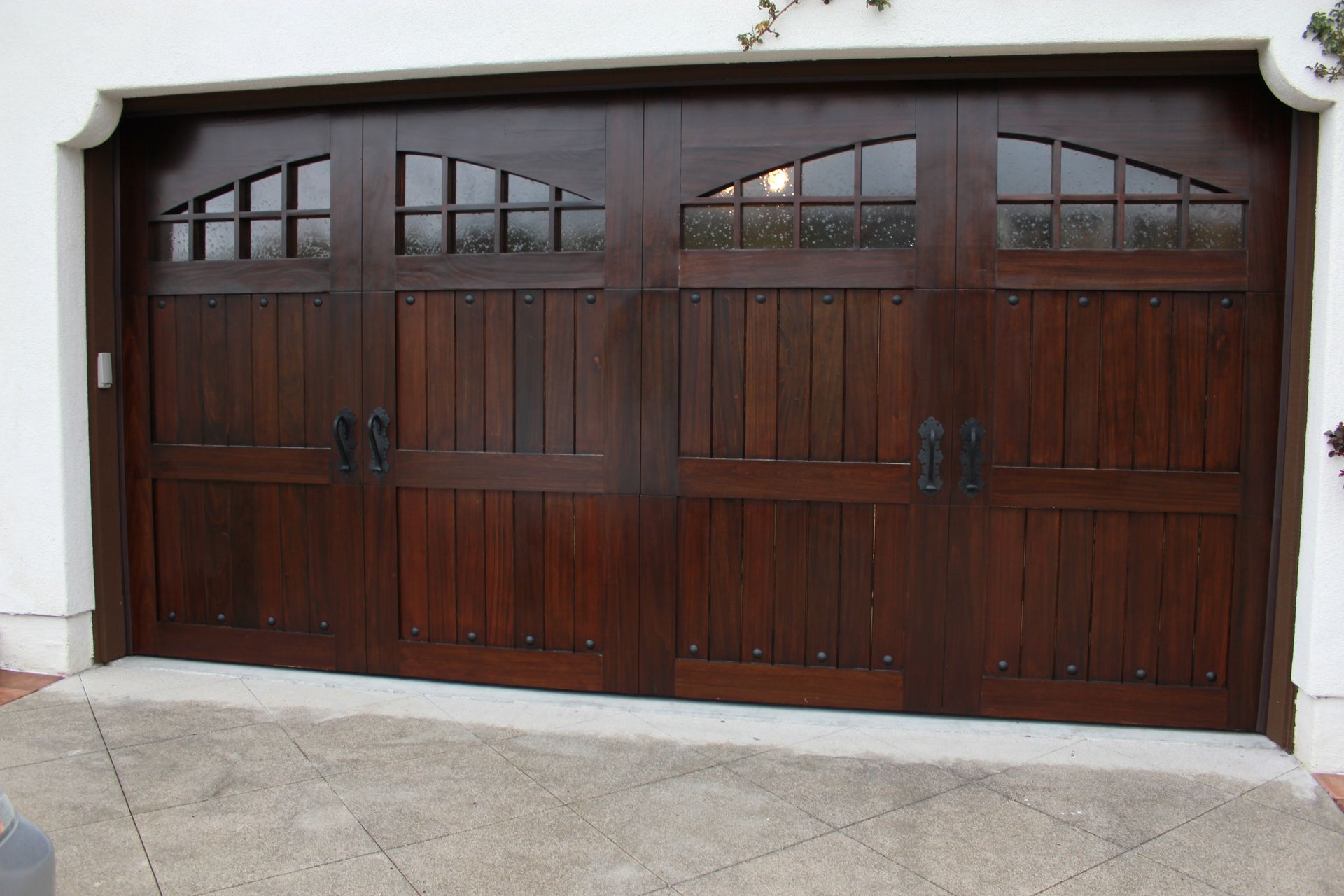 Dark wooden double garage door with arched windows in a white stucco wall