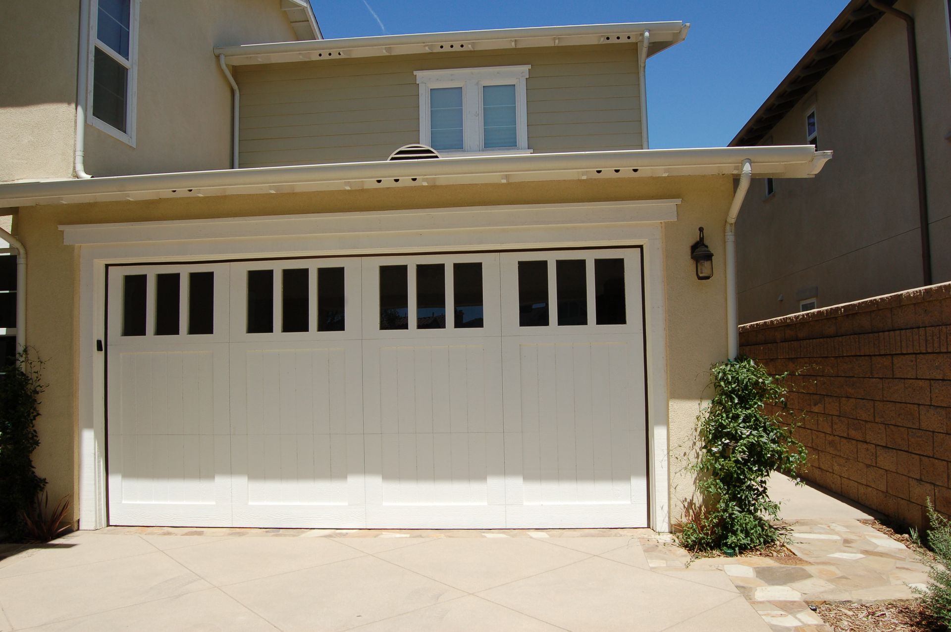 Suburban house exterior with white garage door, beige siding, and driveway under bright sun