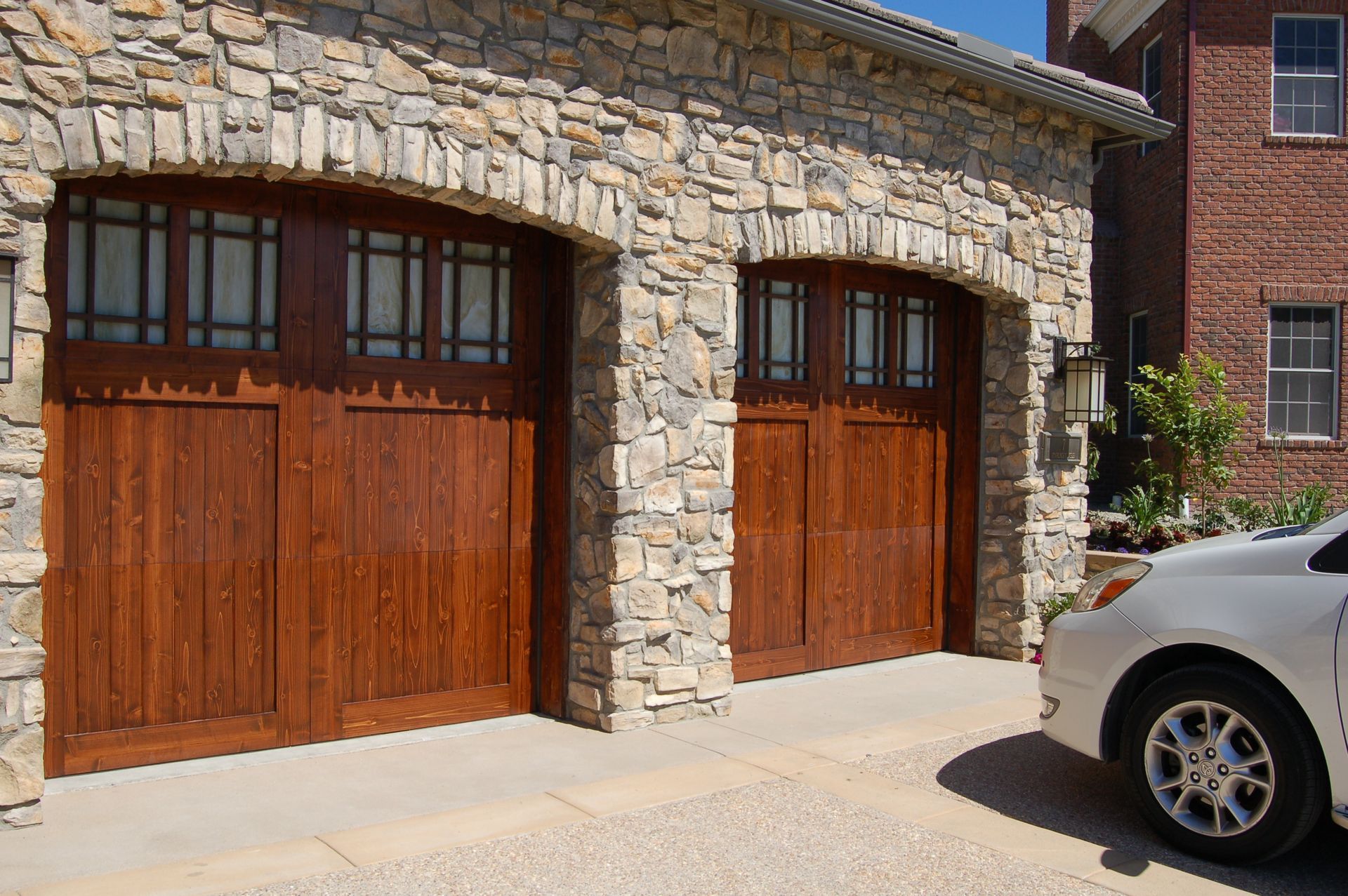 Stone garage with two wooden doors beside a parked silver car under bright sunlight