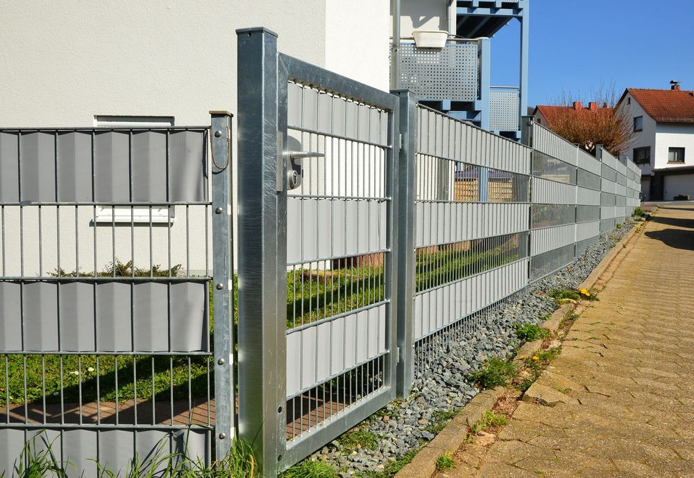 Gray metal fence along a sidewalk beside a residential building on a sunny day