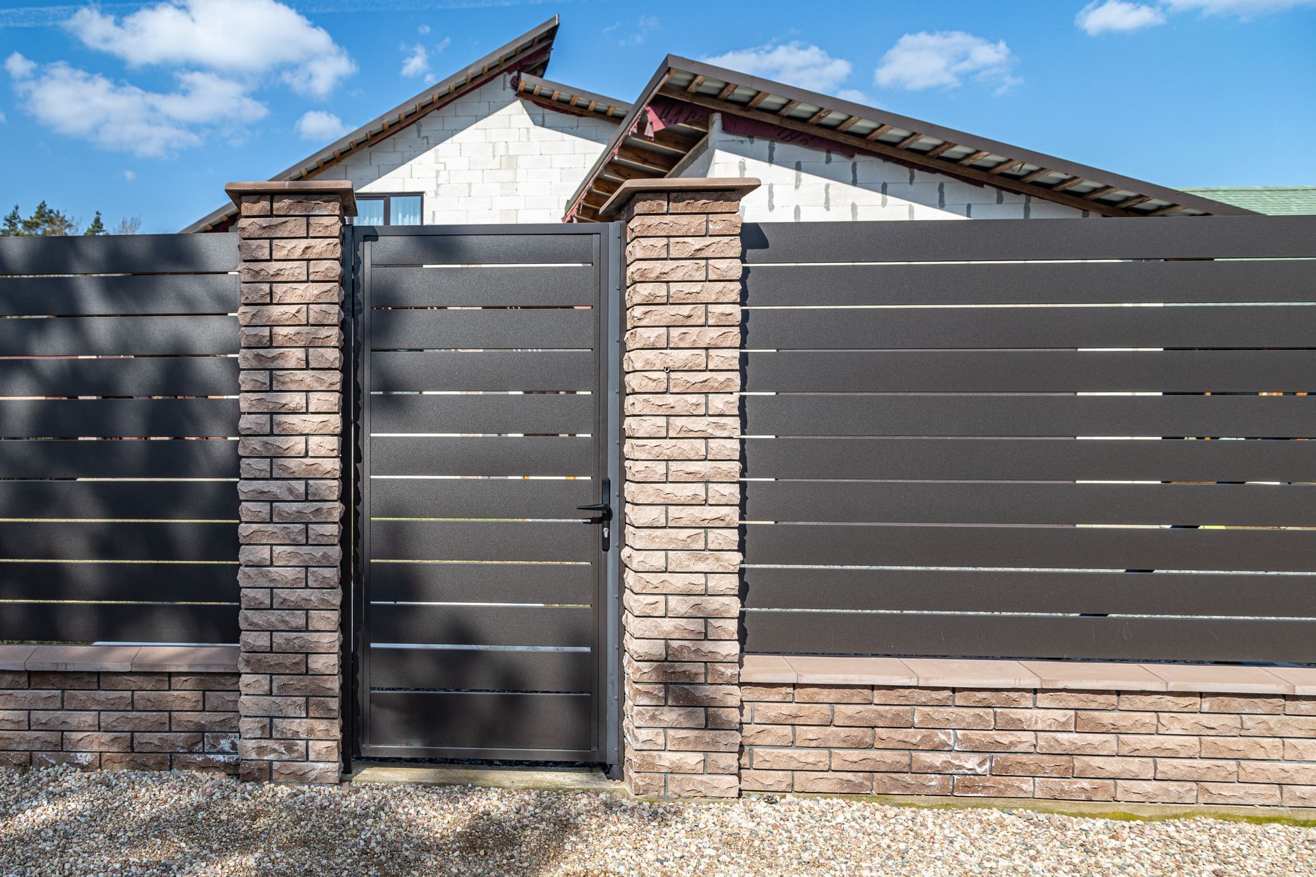 Modern house exterior with a black metal gate and beige brick fence under a blue sky
