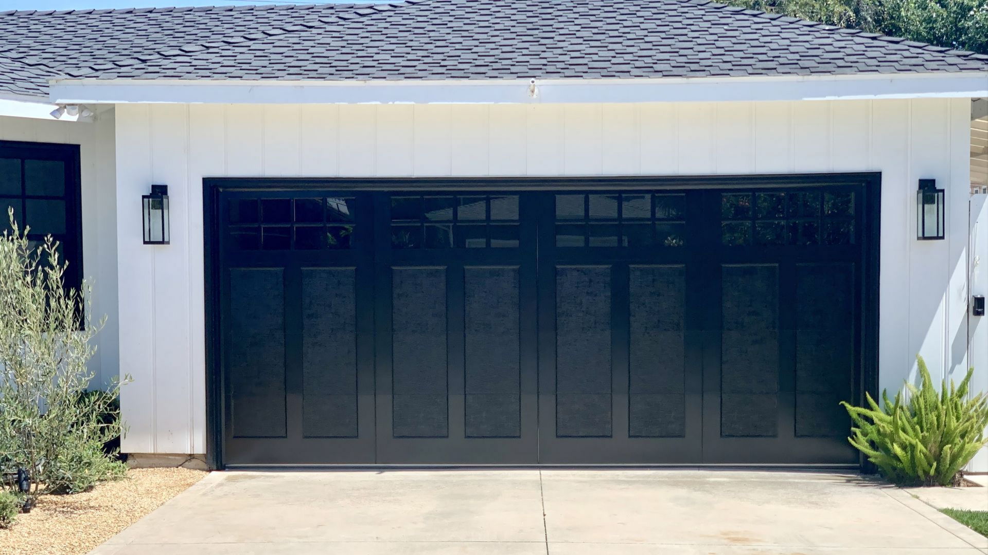 Black double garage door on a white suburban house with driveway and small landscaping plants