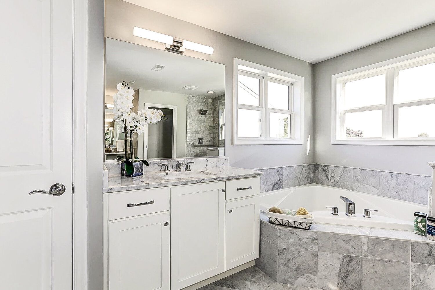 A bathroom with a tub , sink , mirror and window.