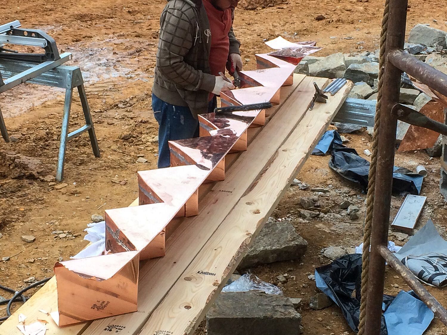 A man is working on a copper staircase on a wooden table.