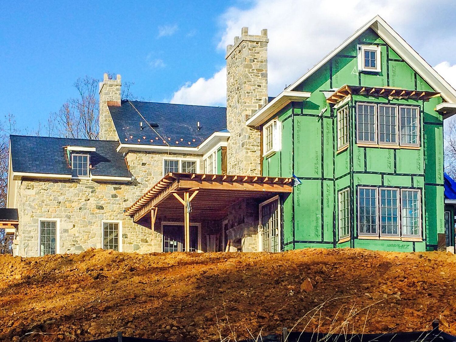 A large house is being built on top of a dirt hill.