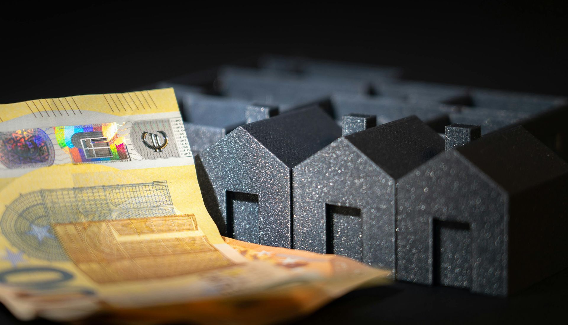 Euro banknotes next to a row of miniature house figures, symbolizing real estate and finance.