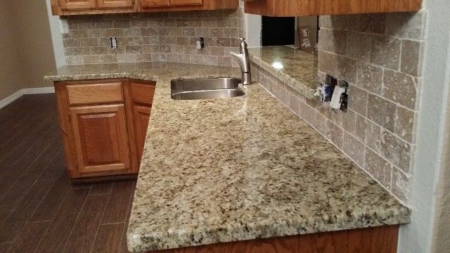 Kitchen countertop with granite surface, wood cabinets, tiled backsplash, and stainless sink.