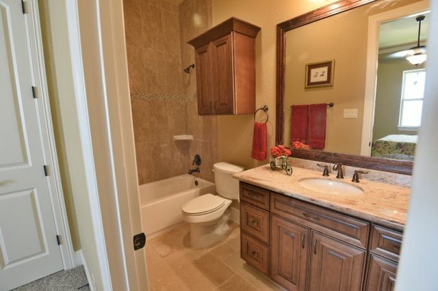 Bathroom with vanity, mirror, toilet, and wood cabinets in beige tile finish