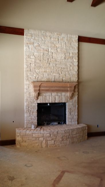 Stone fireplace with wooden mantel in a beige room with a high ceiling