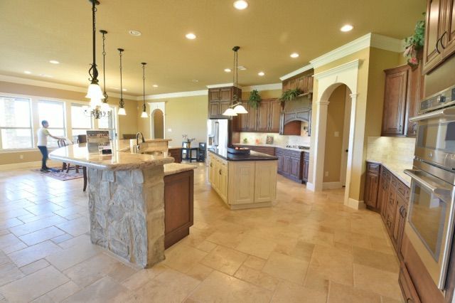 Spacious modern kitchen with stone island, tan tile floors, and built-in appliances