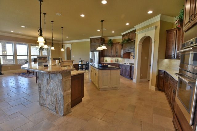 Spacious modern kitchen with stone island, tan tile floor, and pendant lights
