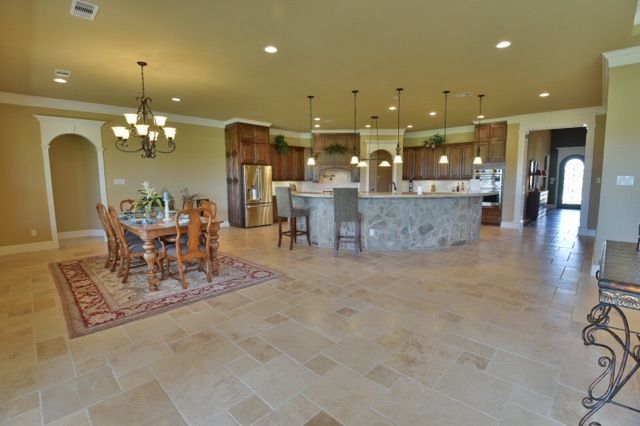 Spacious tiled kitchen and dining area with a stone island, wood cabinets, and chandelier lighting.