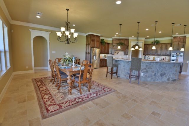 Spacious beige kitchen and dining area with a round table, chandelier, and marble island.