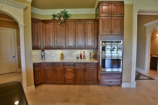 Spacious kitchen with dark wood cabinets, beige tile floor, stainless oven, and arched entryways.