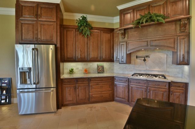 Modern kitchen with stainless steel fridge, wooden cabinets, and tan tile floor
