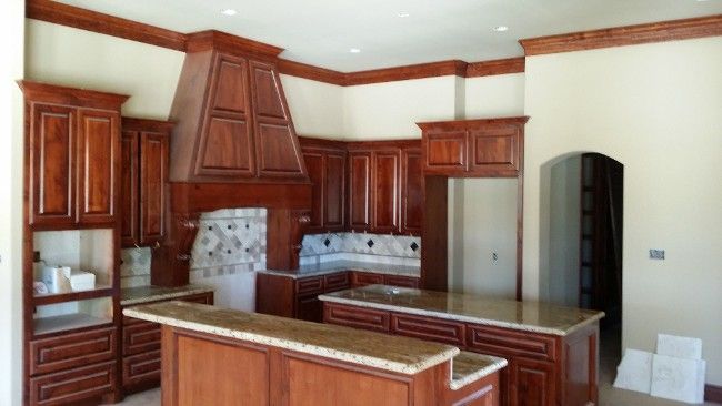 Spacious kitchen with cherry wood cabinets, granite island, stainless refrigerator, and decorative range hood