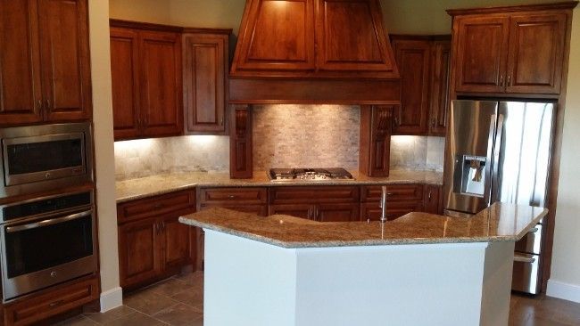 Modern kitchen with dark wood cabinets, granite island, built-in ovens, and stainless steel refrigerator.