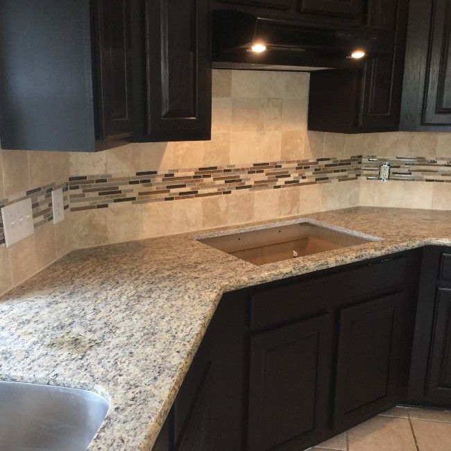 Corner kitchen countertop with speckled granite, dark cabinets, tile backsplash, and a sink cutout
