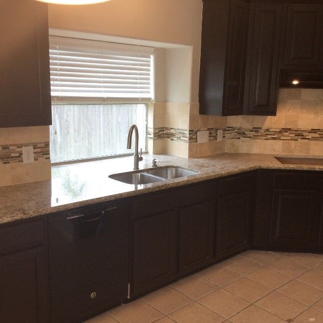 Modern kitchen with dark cabinets, granite counters, tiled floor, and a window above the sink.