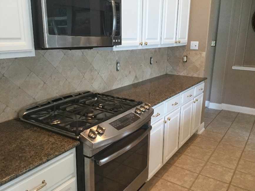 Modern kitchen with stainless steel stove, microwave, white cabinets, and tiled floor
