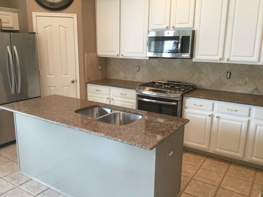 Modern kitchen with white cabinets, stainless steel appliances, and granite island with double sink