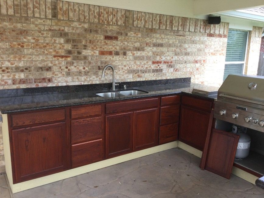 Outdoor kitchen with brick backsplash, dark countertop, sink, and grill