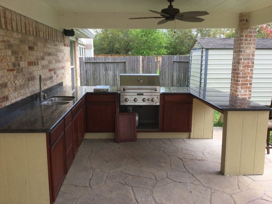 Outdoor covered patio with built-in grill, sink, and dark countertops on brick pillars