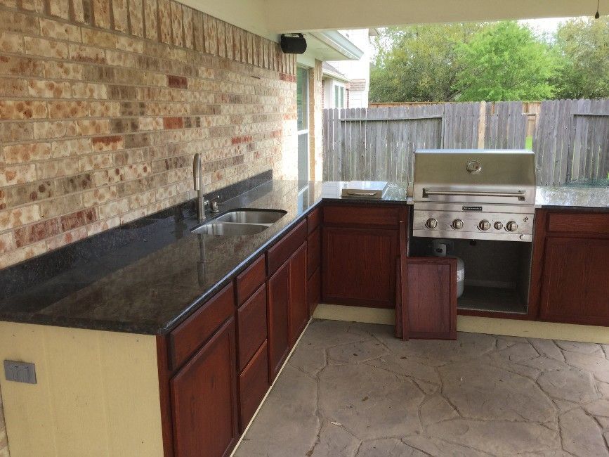 Outdoor patio kitchen with dark countertops, brick wall, and stainless steel grill