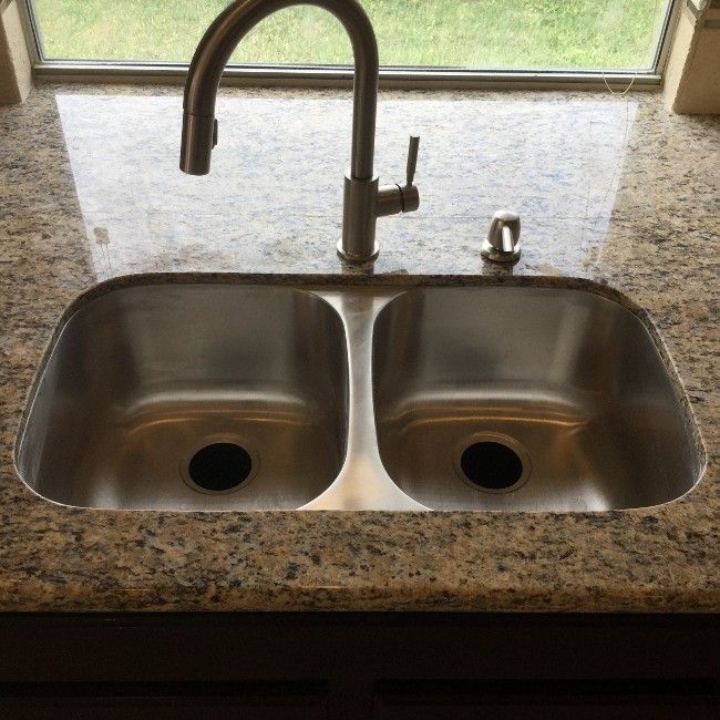 Double stainless steel kitchen sink with a curved faucet and speckled granite countertop.