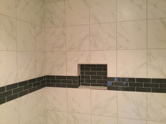 Tiled bathroom wall with a black accent stripe and a small recessed niche.