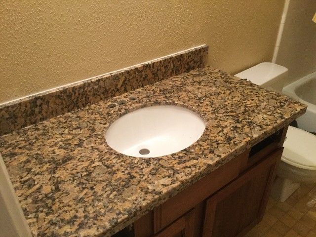 Granite bathroom countertop with white sink and wooden vanity beside a toilet