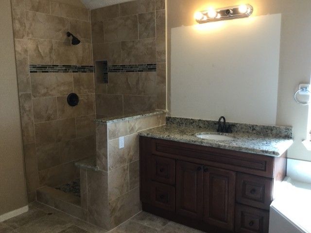 Modern bathroom with tiled walk-in shower, granite vanity, and wall sconce lighting