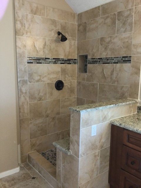 Tiled walk-in shower with bench, corner shelf, showerhead, and glass partition beside a vanity.
