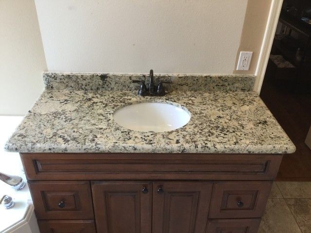 Bathroom vanity with granite countertop, white sink, and dark wood cabinet against a white wall