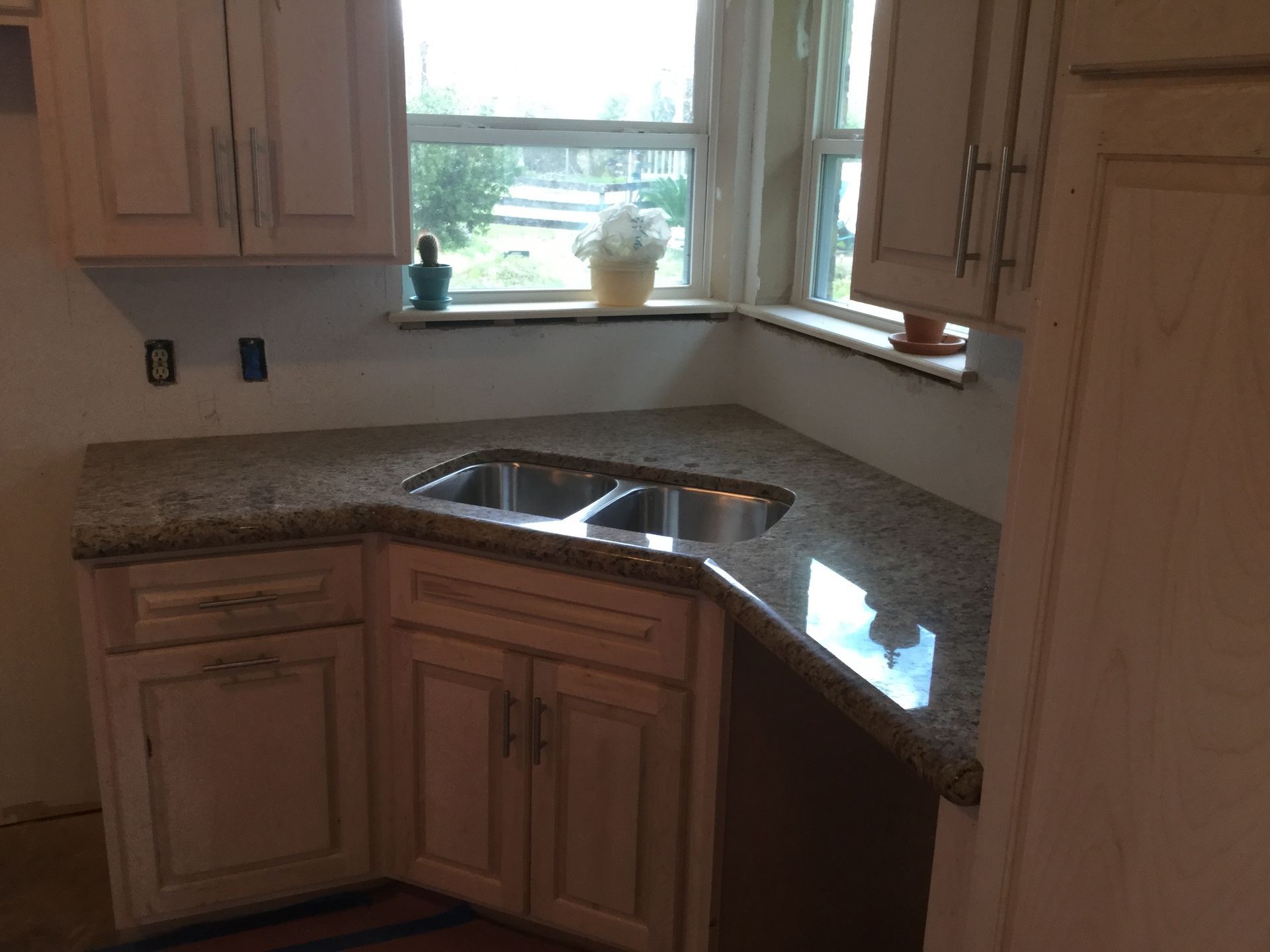 Corner kitchen sink with double basin, wood cabinets, and granite countertops by a sunlit window