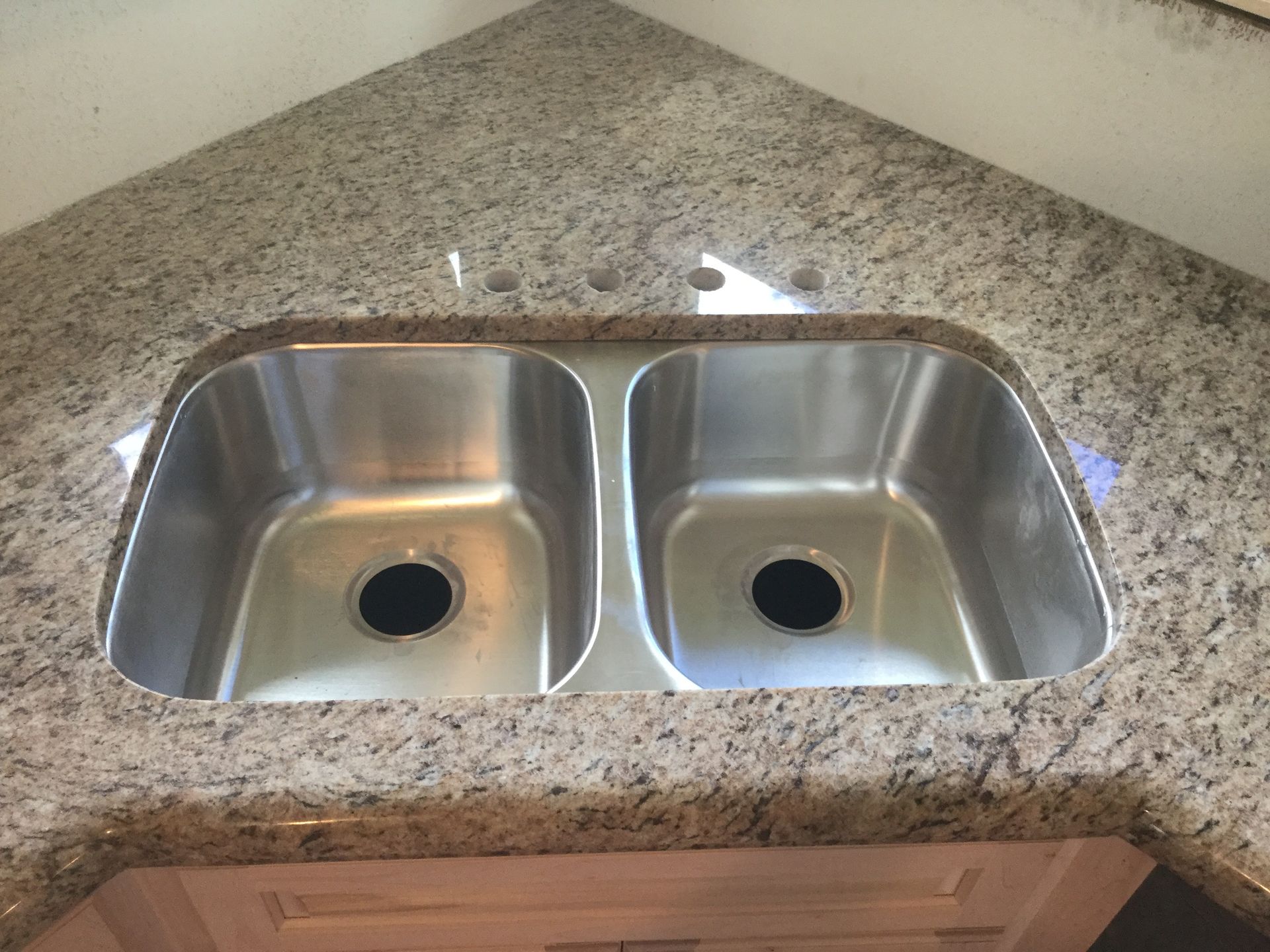 Double stainless steel kitchen sink set in speckled granite countertop with wooden cabinets below