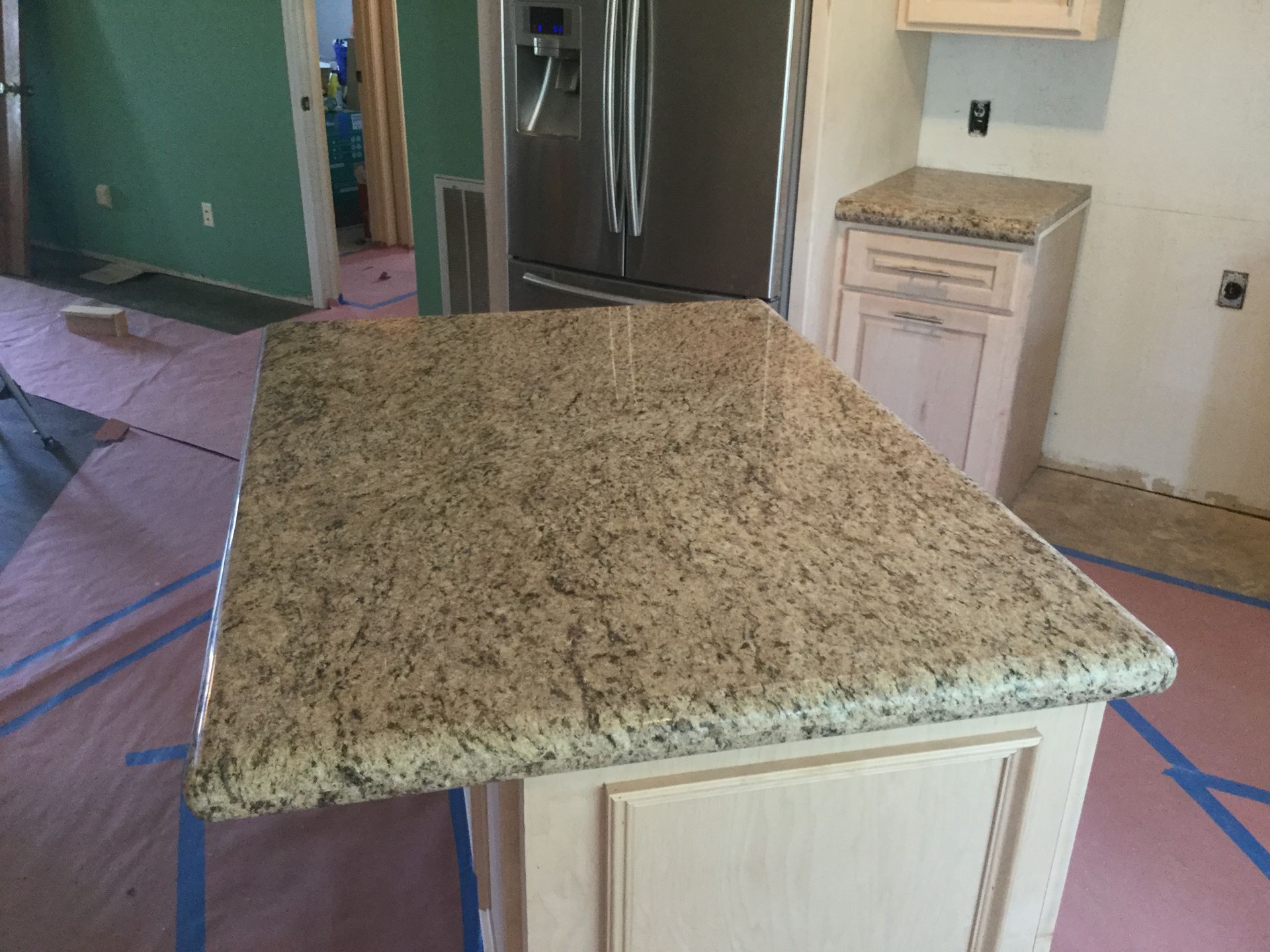 Kitchen island with speckled granite countertop and white cabinet base in a partially renovated room