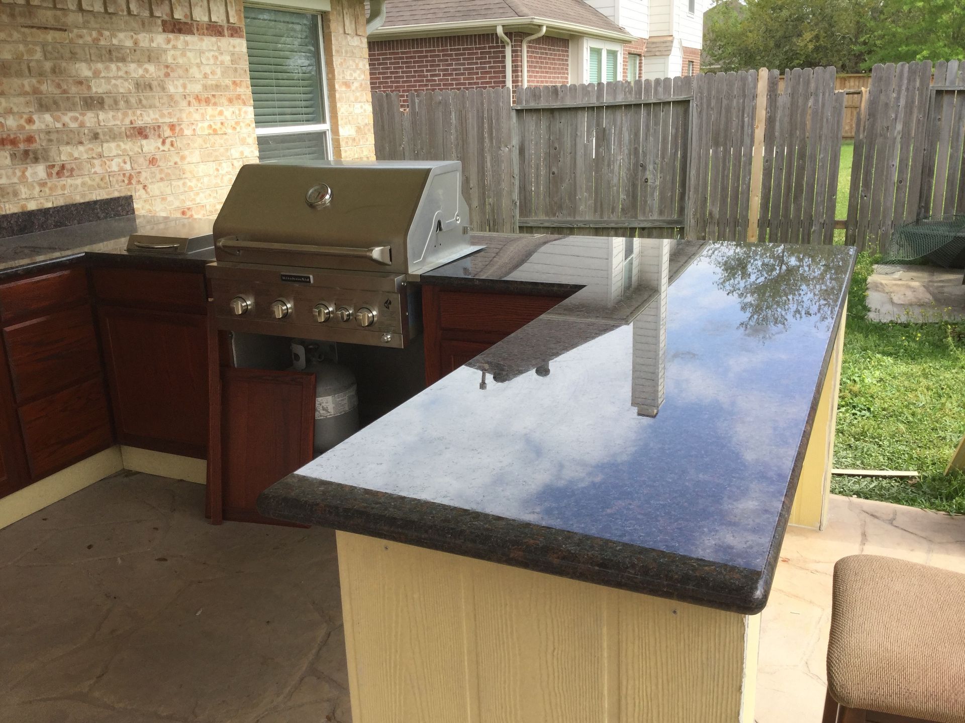 Outdoor patio with built-in grill and black granite countertop beside a fenced backyard