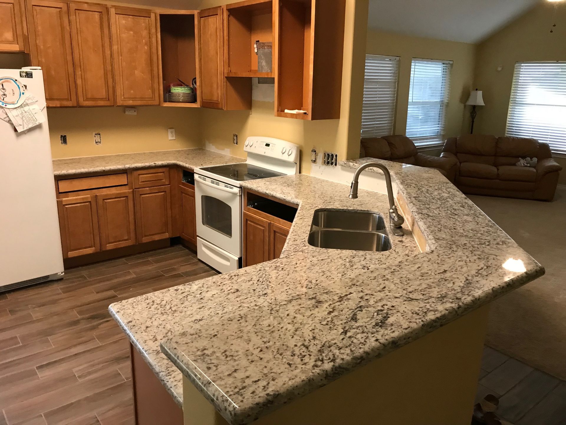 Kitchen with wood cabinets, granite island sink, white appliances, and a living room in the background