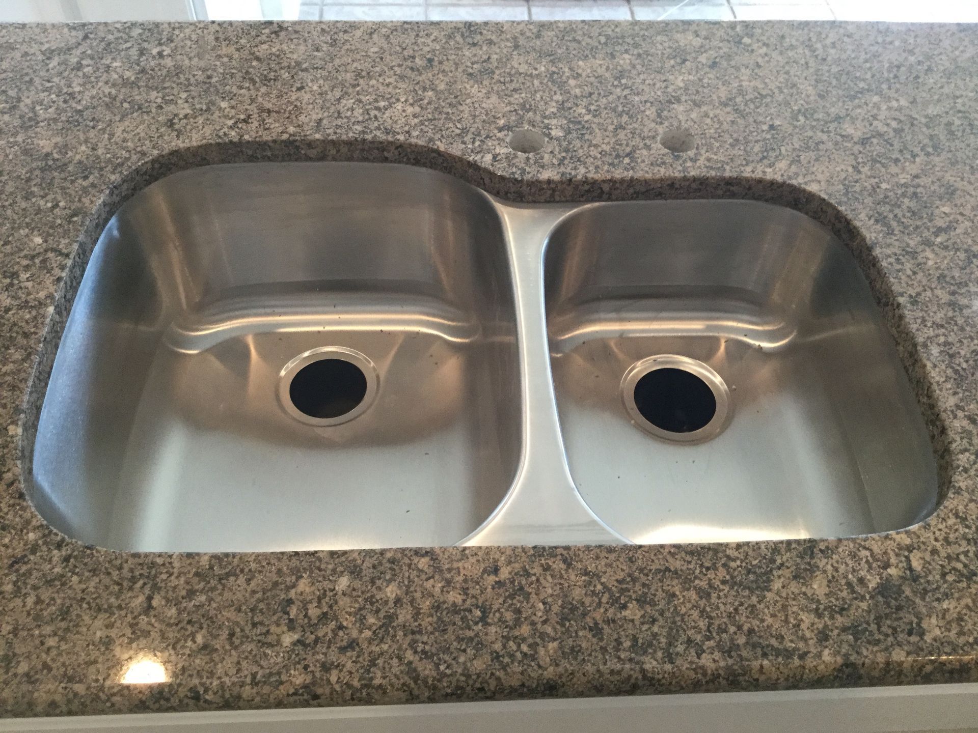 Double-basin stainless steel kitchen sink set in speckled granite countertop
