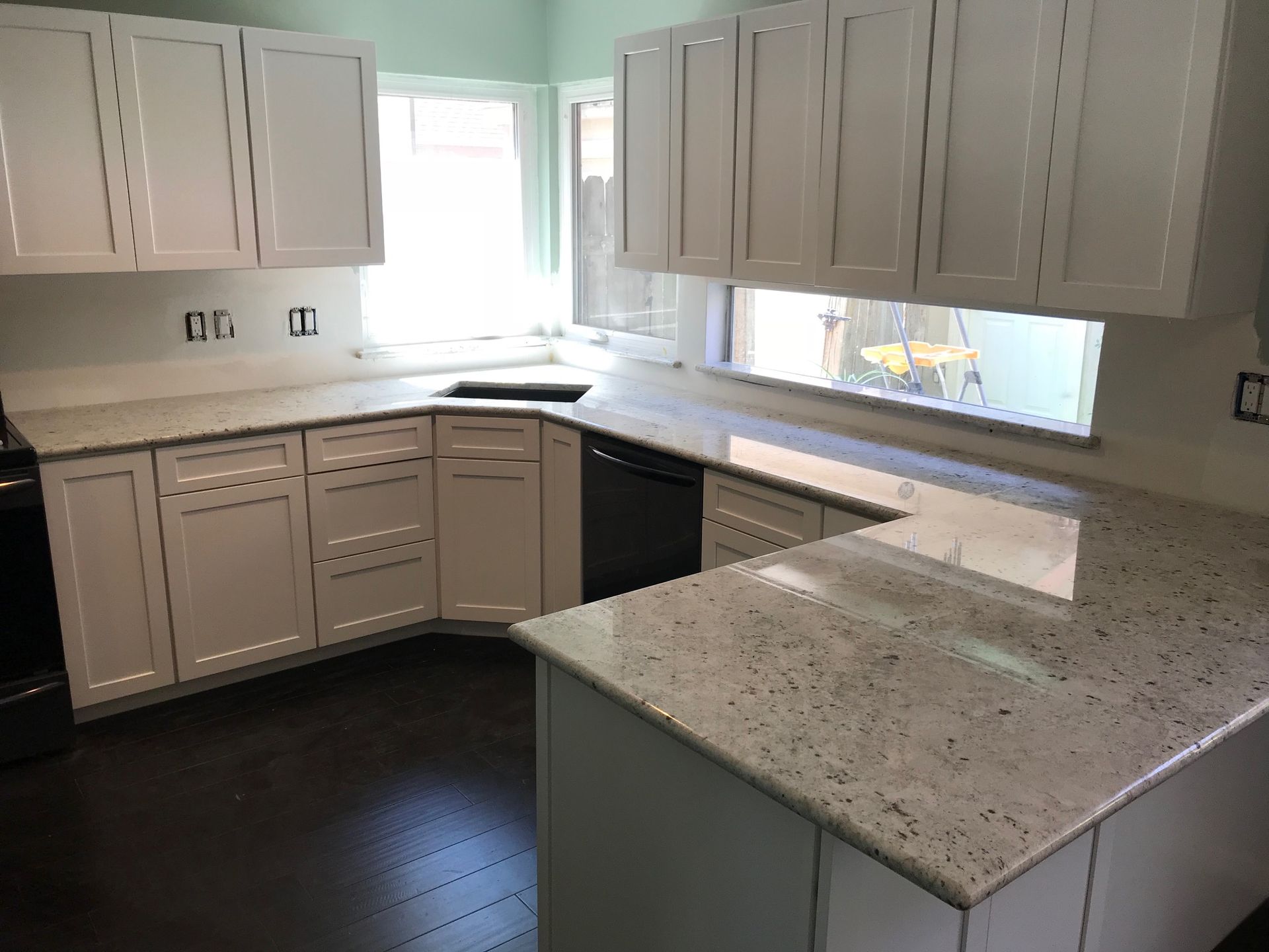 Bright white kitchen with gray cabinets, speckled countertops, and dark wood flooring.