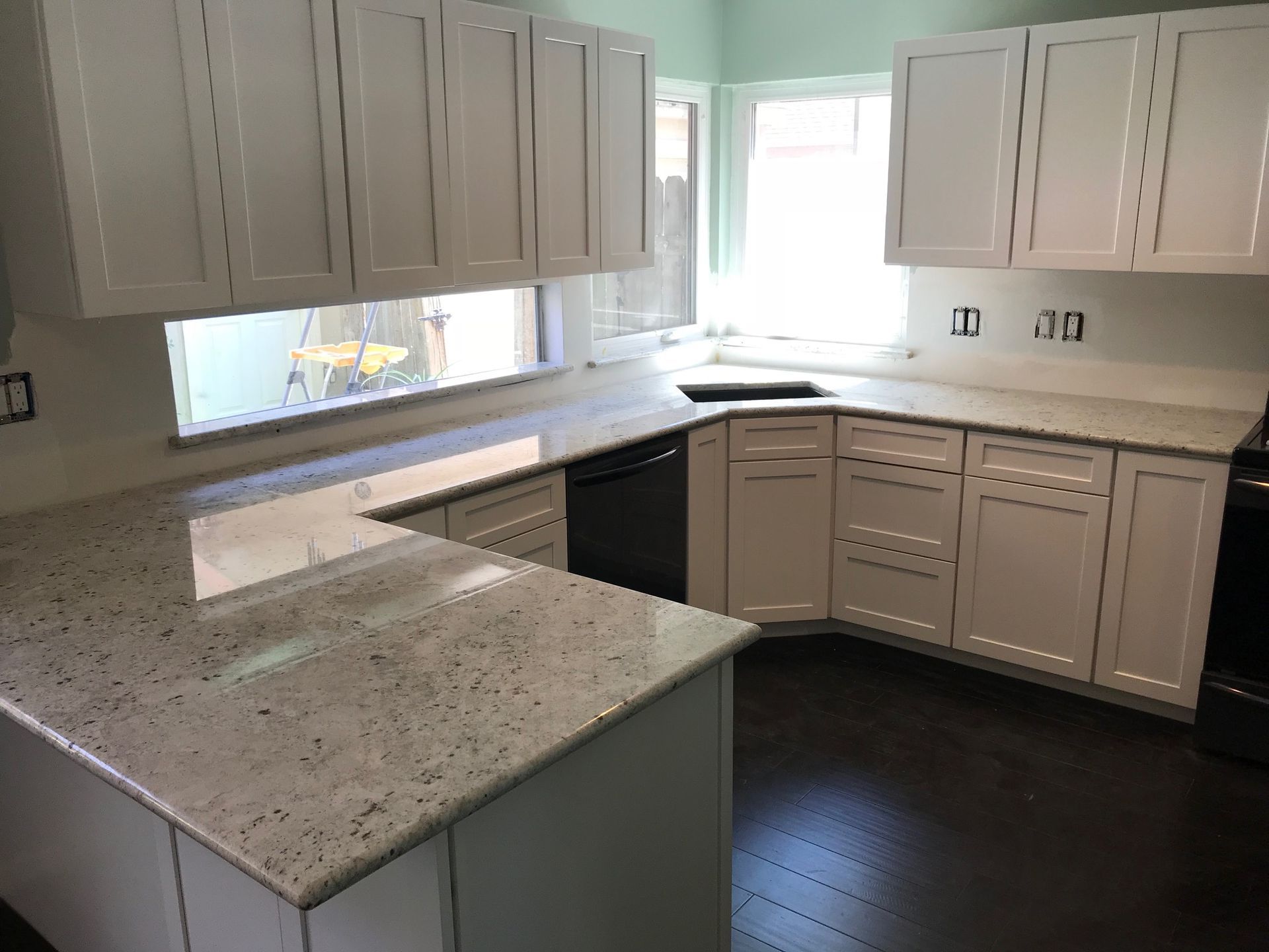 Bright kitchen with white cabinets, speckled granite counters, and dark wood flooring