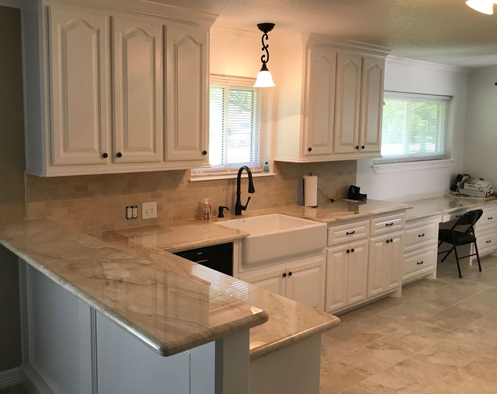 Bright kitchen with white cabinets, tan countertops, sink, window, and pendant light.